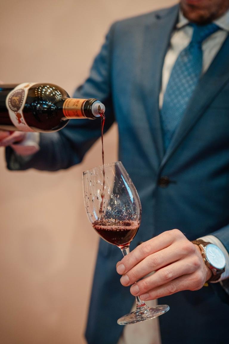 Wine being poured into a glass by a man in a blue suit, showcasing fine dining and elegance.