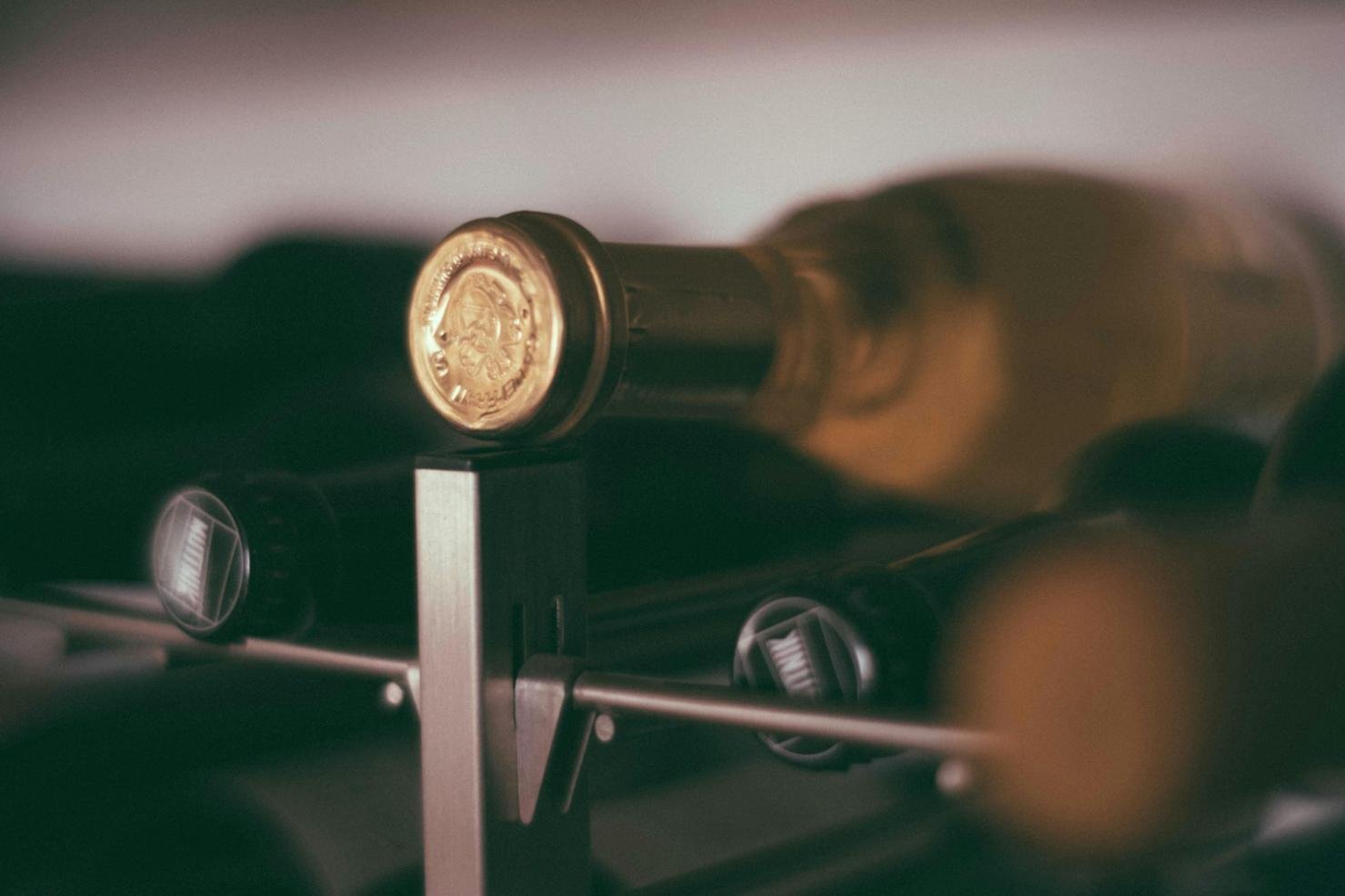 Close-up of wine bottles stored in a wine rack, showcasing the bottle caps and subtle lighting.