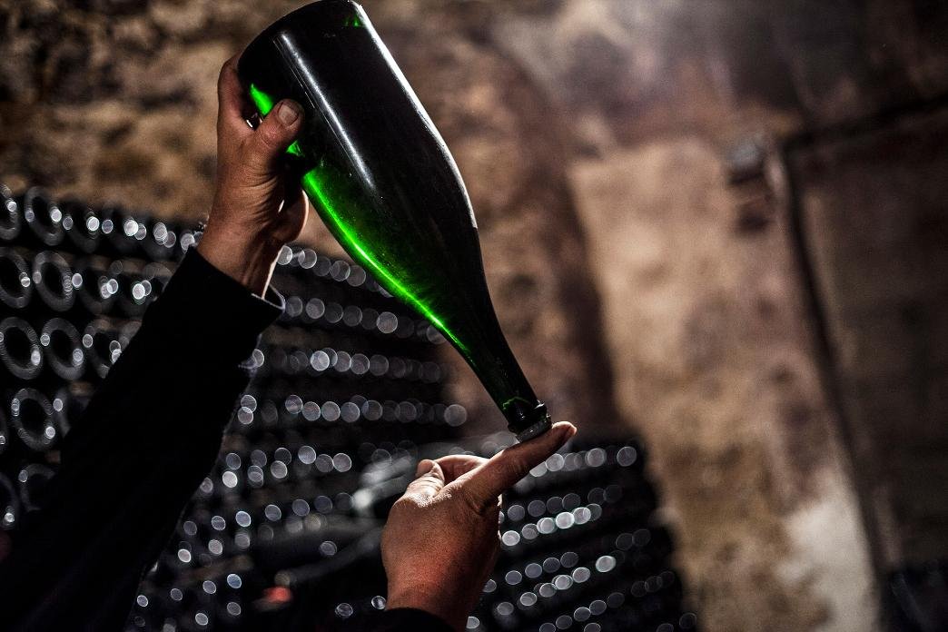 Winemaker inspecting wine bottle in a cellar, checking clarity and sediment before corking.