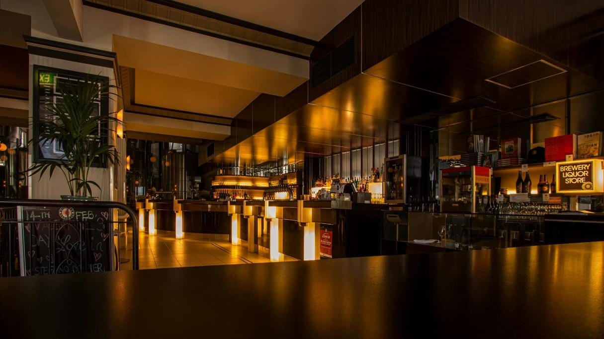 Modern, dimly-lit bar interior with sleek design, warm lighting, and a well-stocked counter. Cozy and sophisticated atmosphere.